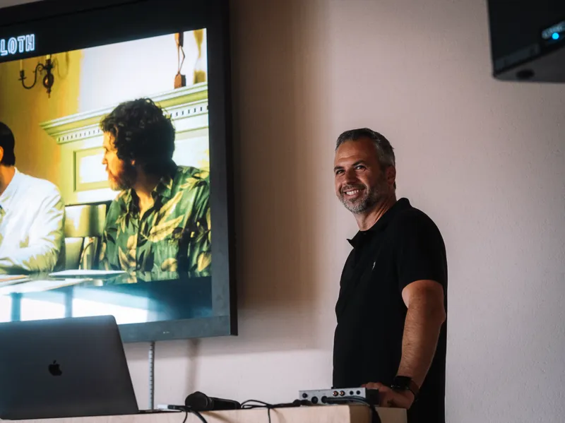 Brad Hasse on stage at FABRICA, with a scene from Songs for a Sloth on the screen behind him